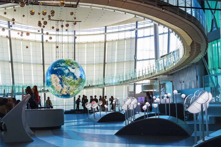 People in the vast lobby of a museum with a planet Earth suspended from a circular ceiling.