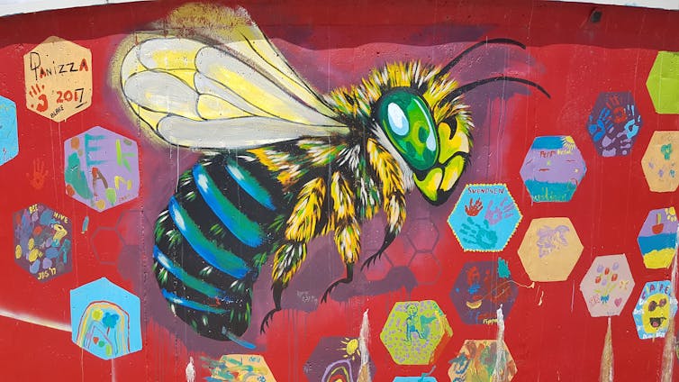 A photo of a mural depicting an enormous blue-banded bee on a red background