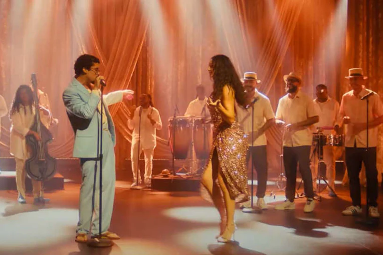 Un hombre canta delante de una banda de salsa mientras mira a una mujer que baila