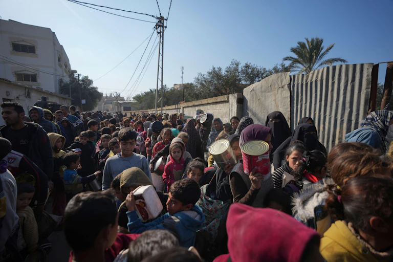 People queue for food holding empty containers in Deir al-Balah, Gaza Strip