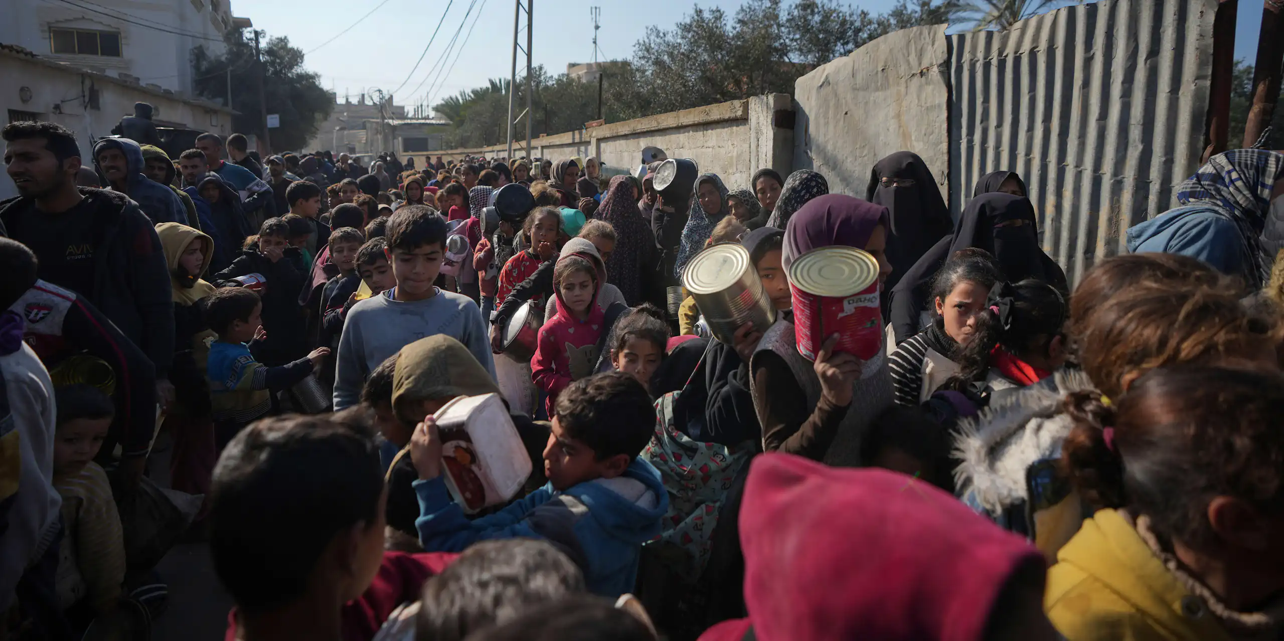 People queue for food holding empty containers in Deir al-Balah, Gaza Strip