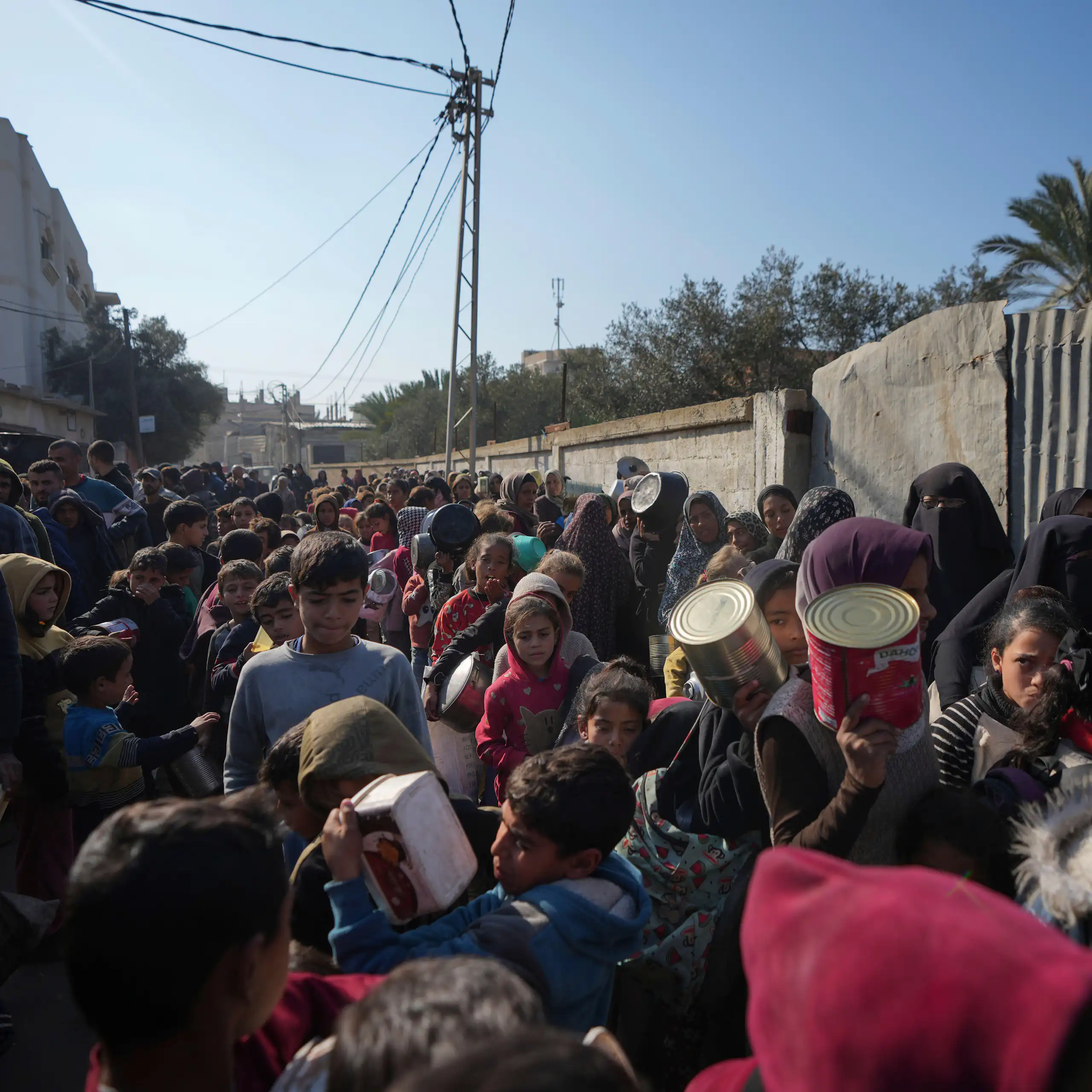 People queue for food holding empty containers in Deir al-Balah, Gaza Strip