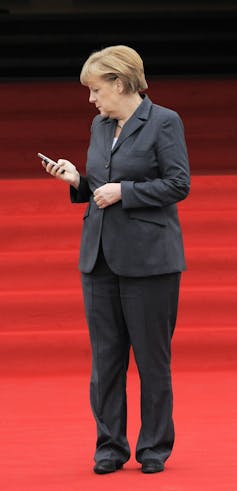 A woman with short dark-blond hair in a grey suit looks down at her phone.