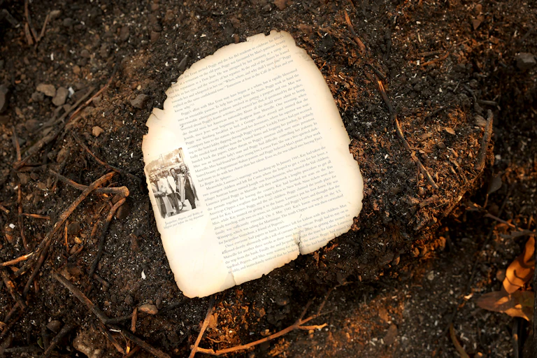 A loose page with text, a black-and-white photo and seared borders sits on orange-hued rubble and dirt.