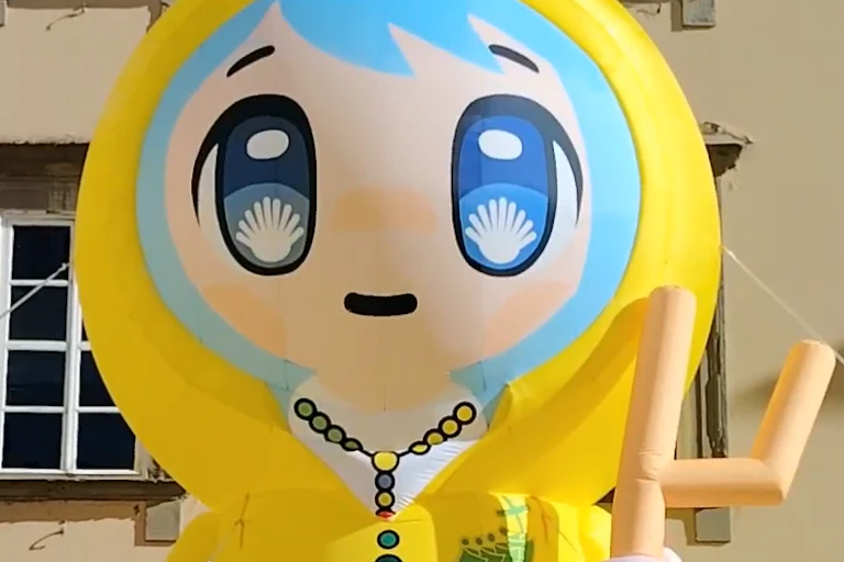 An inflatable cartoon depicts a girl wearing rosary beads with a crucifix, and scallop shells in her eyes.