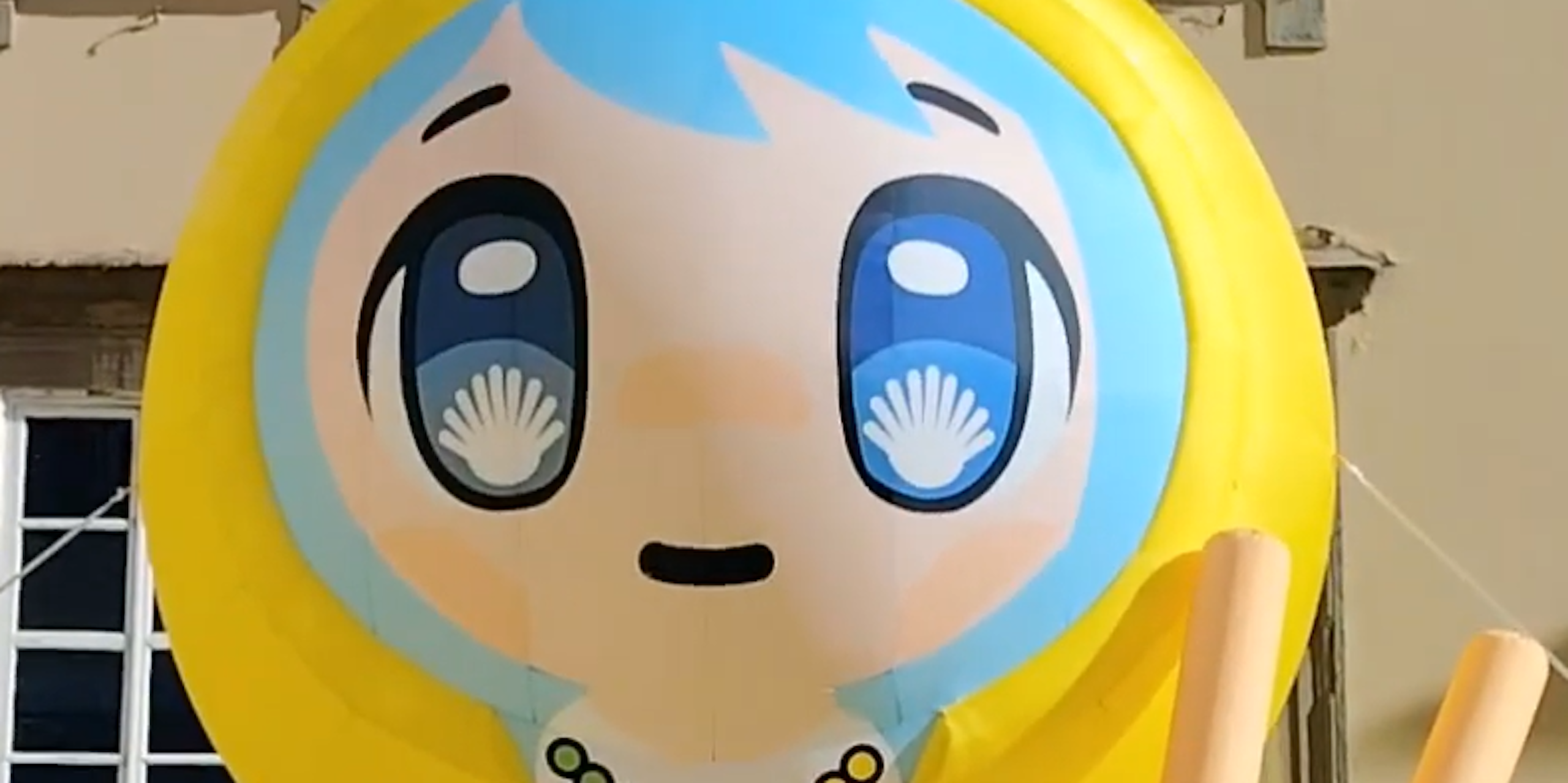 An inflatable cartoon depicts a girl wearing rosary beads with a crucifix, and scallop shells in her eyes.