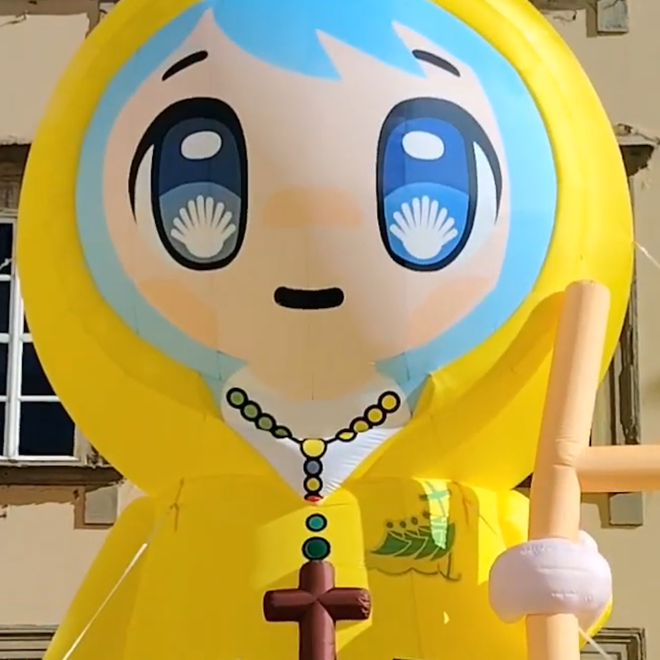 An inflatable cartoon depicts a girl wearing rosary beads with a crucifix, and scallop shells in her eyes.