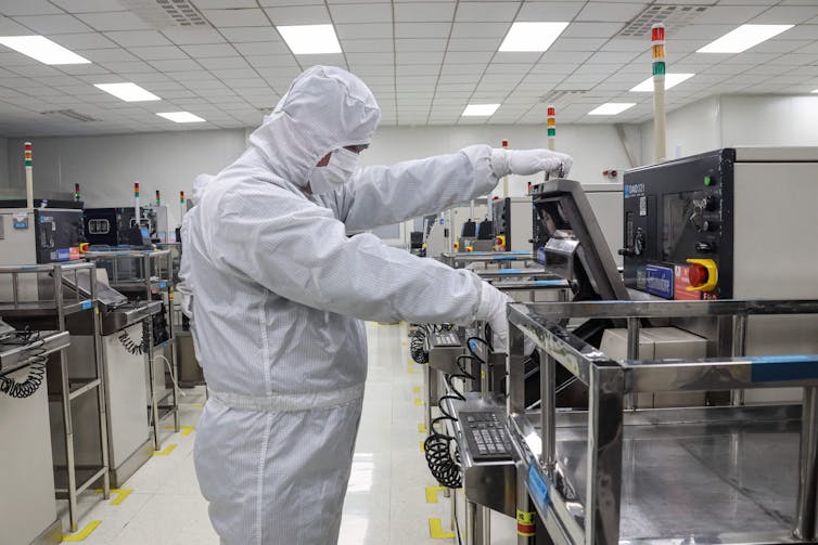 A man in a white hazmat suit works at a desk.