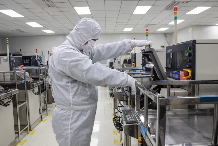 A man in a white hazmat suit works at a desk.