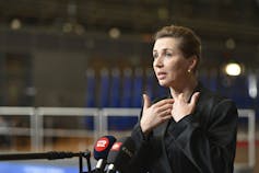 A woman with dark hair pulled back gestures as she speaks.