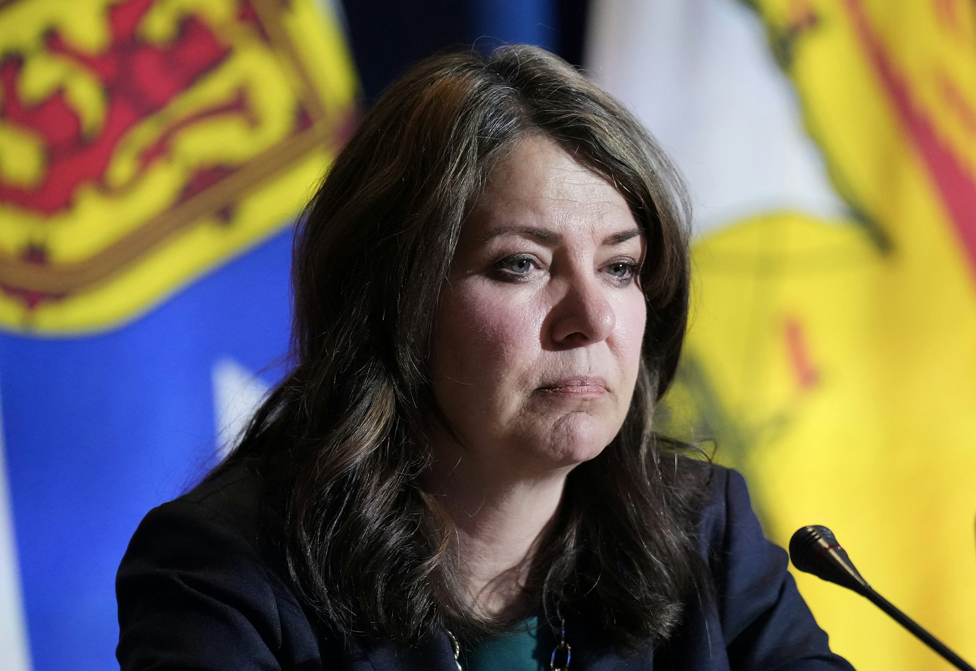 A woman with dark hair looks glum in front of a microphone.