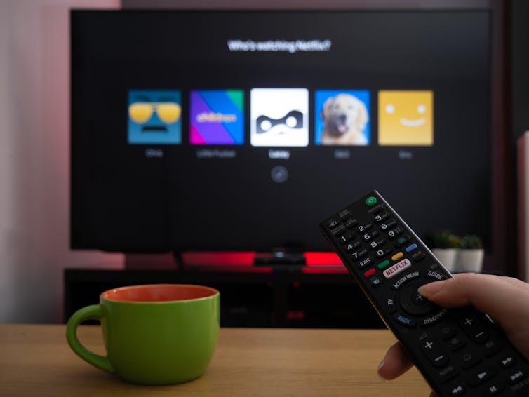 Person holding remote, screen shows a streaming service loading screen