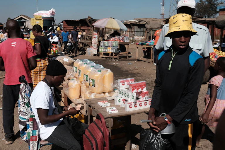 Roadside vendors sell goods at tables.