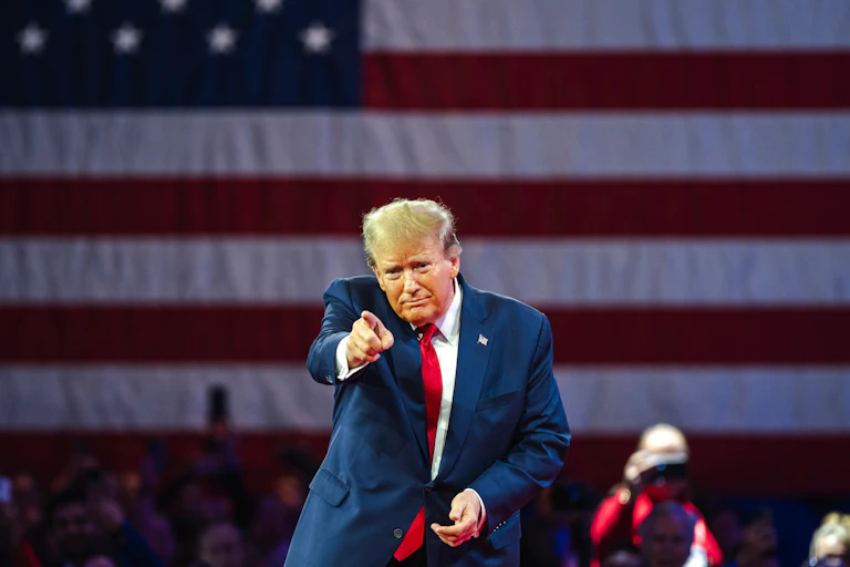 Donald Trump pointe du doigt derrière lui un drapeau américain
