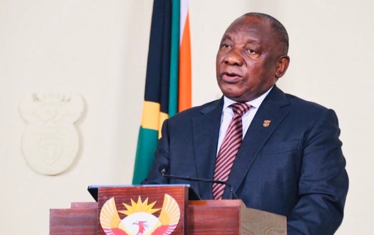 President Cyril Ramaphosa, wearing a suit and tie, speaks at a podium with the South African coat of arms.