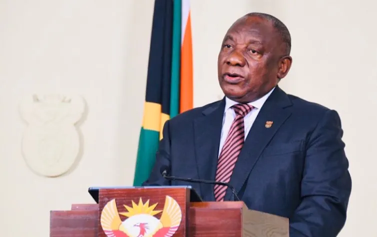 President Cyril Ramaphosa, wearing a suit and tie, speaks at a podium with the South African coat of arms.