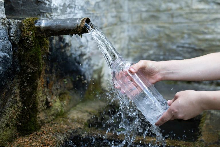Person filling water bottle from a stream coming out of a pipe embedded in a wall