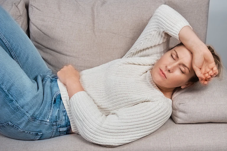 A woman, with one arm across her forehead and the other on her stomach, lies on a couch.