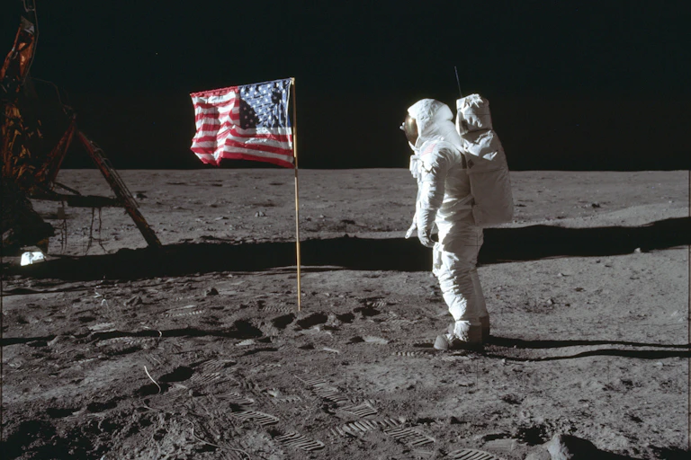 Astronaut Buzz Aldrin in a spacesuit on the lunar surface next to an American flag.