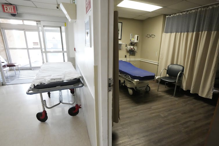 Two empty hospital beds in a room and a hallway near the entrance