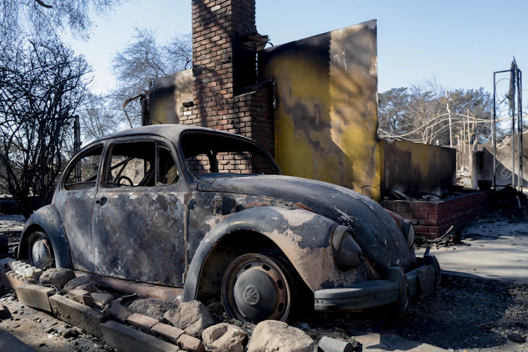 A burned-out car is parked in front of a house devastated by fire.