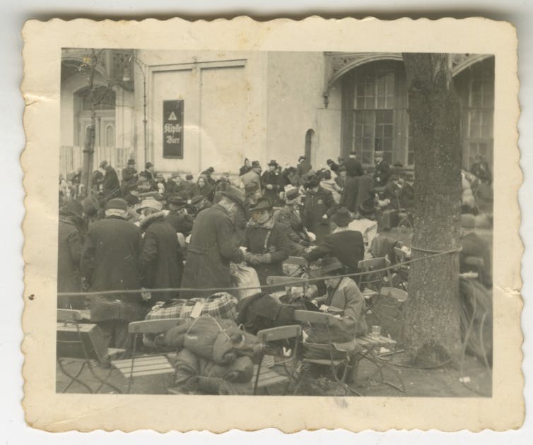 Large group of people wearing Jewish stars gather outdoors, carrying bundles of their belongings