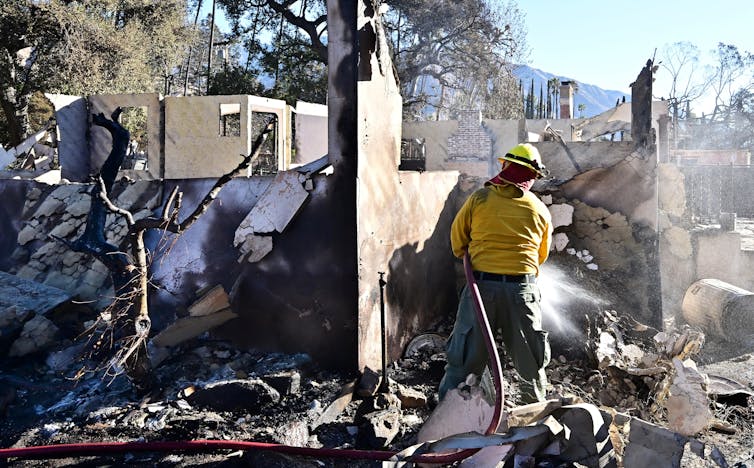 Firefighters spray down the rubble of burned homes.