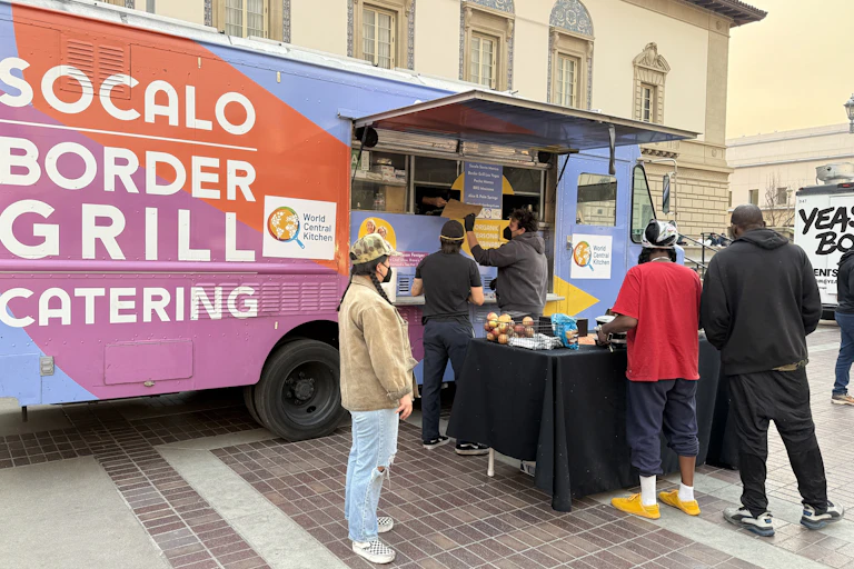 People in face masks get something to eat from a food truck.