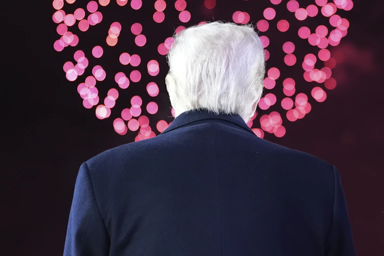 A white-haired man and a woman with dark-blond hair have their backs to the camera as they look at pink and red fireworks.