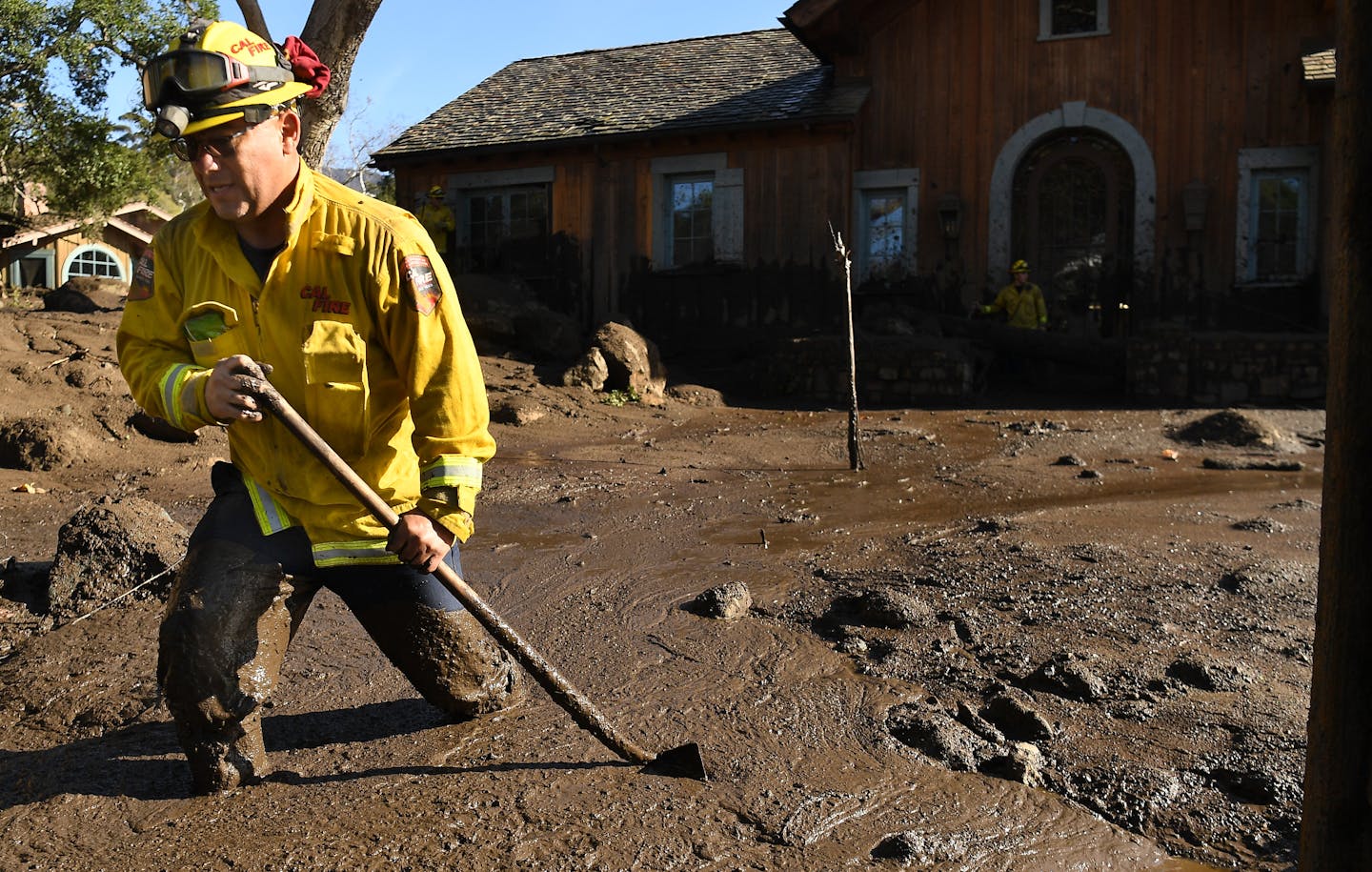A firefighter stands knee-deep in mud in a yard in front of a home.