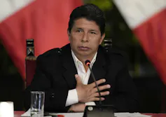 A man holds his hand to his chest; a microphone sits in front of him.
