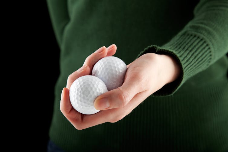 A hand holding two golf balls.
