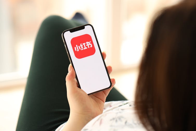 A woman looking at the Xiaohongshu app on her phone screen.