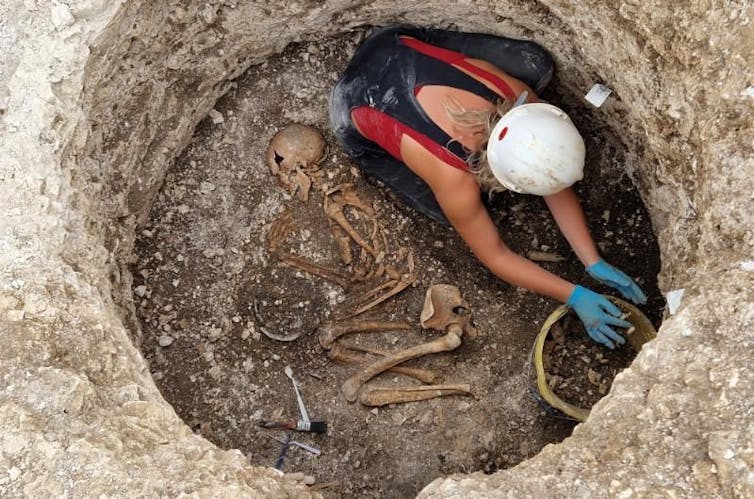 A woman in a pit digging next to a skeleton