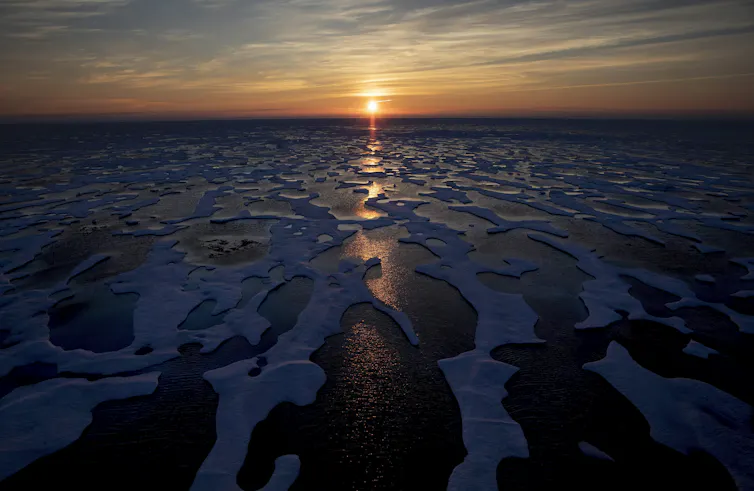 The midnight sun shines across an expanse of ice-strewn waters.