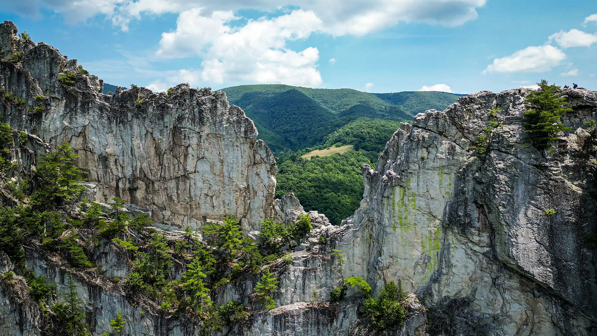 A view through a deep gap in rocks shows forested land beyond.