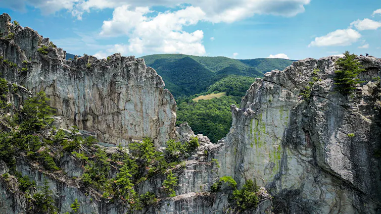 A view through a deep gap in rocks shows forested land beyond.
