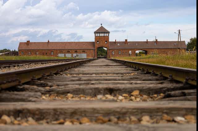 Vue sur une voie ferrée désaffectée, menant à un bâtiment en brique.