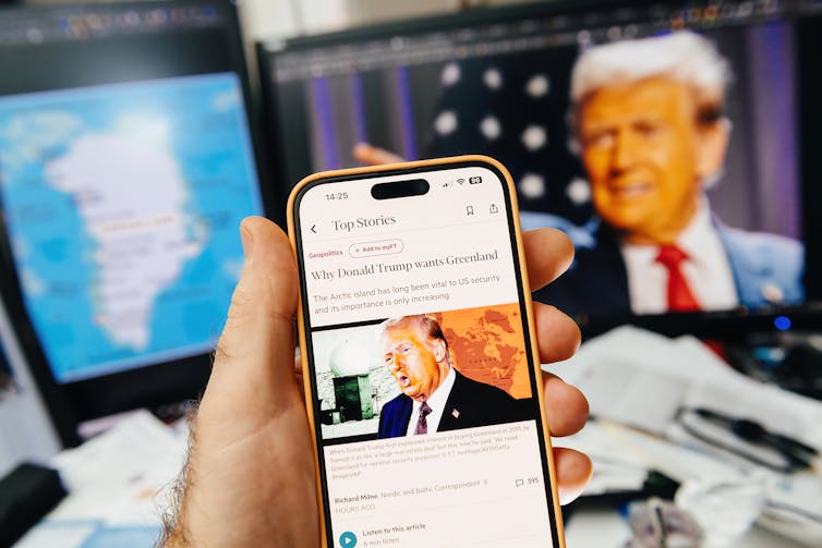 phone screen showing news story about donald trump and greenland in front of a tv screen showing donald trump