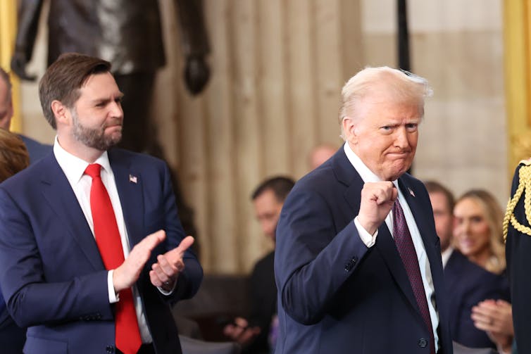 A white man with a blue suit claps his hands and looks at another older white man who pumps his fist.