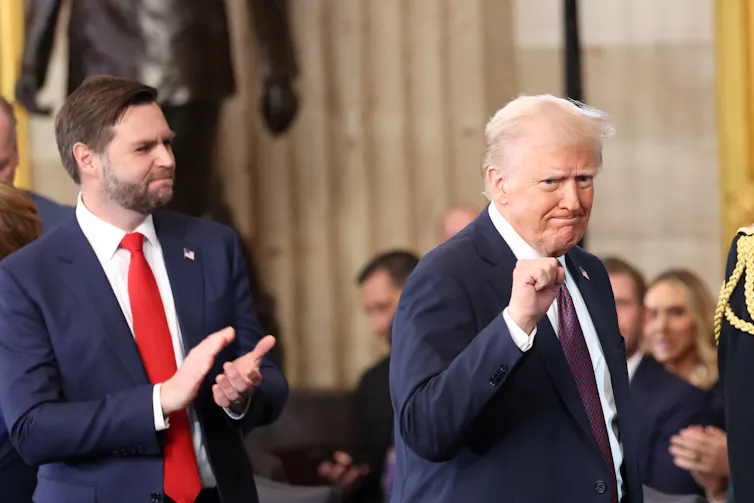 A white man with a blue suit claps his hands and looks at another older white man who pumps his fist.