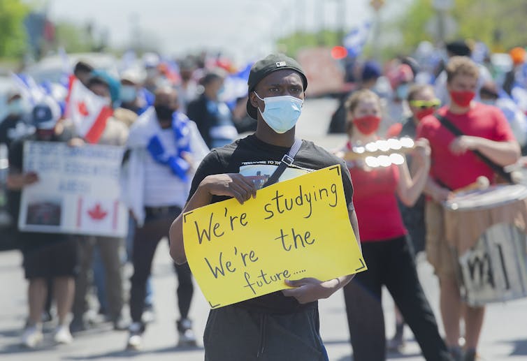 People at a demonstation, one holding a sign that says 'we're studying, we're the future.'