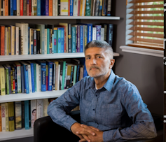 A man sitting in front of a bookcase.