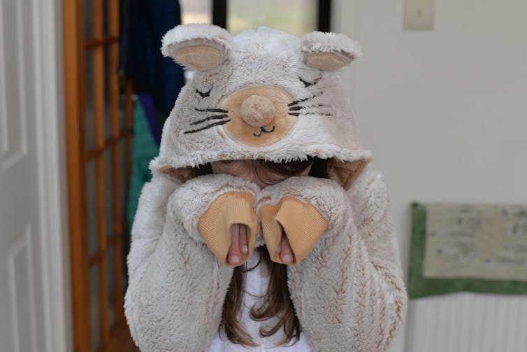 A child in a mouse animal onesie covering their face.