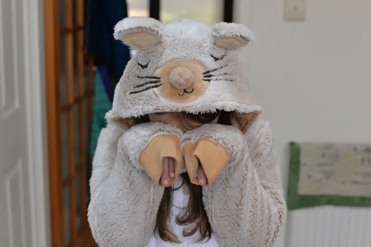 A child in a mouse animal onesie covering their face.