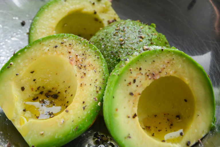 A bowl of sliced avocado drizzled with oil, salt and pepper.