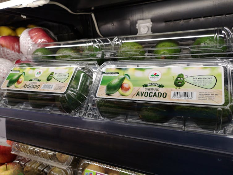 A supermarket shelf with avocados in plastic punnets.
