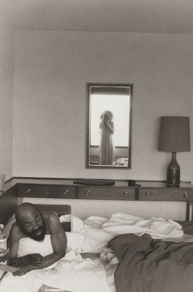 A man in a bed, the photographer in a mirror.
