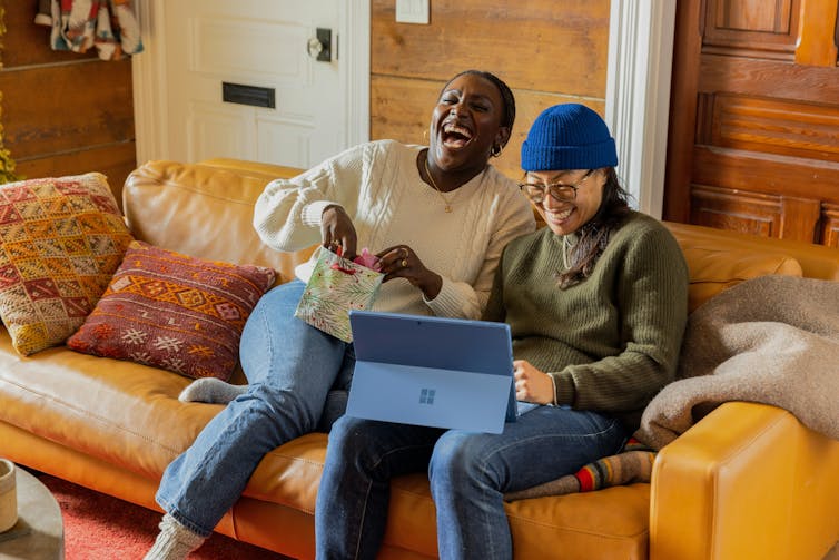 Two women laughing on a sofa with a laptop