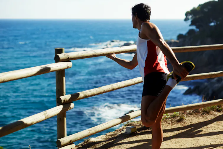 A man stretching his hamstring overlooking the ocean.